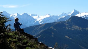 Ein Kind auf einer Almwiese sitzend mit Bergpanorama | © Haus Tannenblick