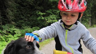 Eine Aufnahme eines Kindes mit Kinder-Fahrrad und Hund auf einem Schotterweg | © Haus Tannenblick