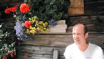 Eine Aufnahme eines Mannes auf einer Bank vor einer Almhütte rastend | © Haus Tannenblick