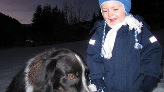 Ein Kind mit seinem Hund spielend im Winter bei Dämmerung | © Haus Tannenblick