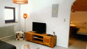 Eine Aufnahme des Wohnbereichs von Appartement 4 - "Schattberg" mit Sofa, Flat-TV und Blick auf den Esstisch in der Küche | © Haus Tannenblick