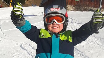 Ein Kind im Skianzug seine Skistöcke in die Luft streckend | © Haus Tannenblick