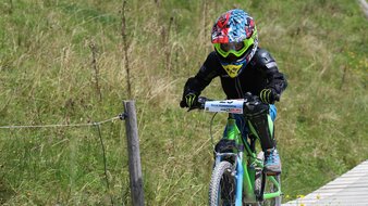 Eine Aufnahme eines Kindes in Mountainbike Montur auf dem Mountainbike einen Trail entlang fahrend | © Haus Tannenblick