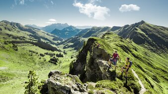 Zwei Wanderer pausieren am Gebirgsgrat während einer Gipfelwanderung bei atemberaubendem Panorama | © saalbach.com - Mia Knoll