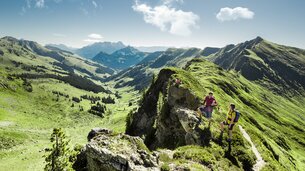 Zwei Wanderer pausieren am Gebirgsgrat während einer Gipfelwanderung bei atemberaubendem Panorama | © saalbach.com - Mia Knoll