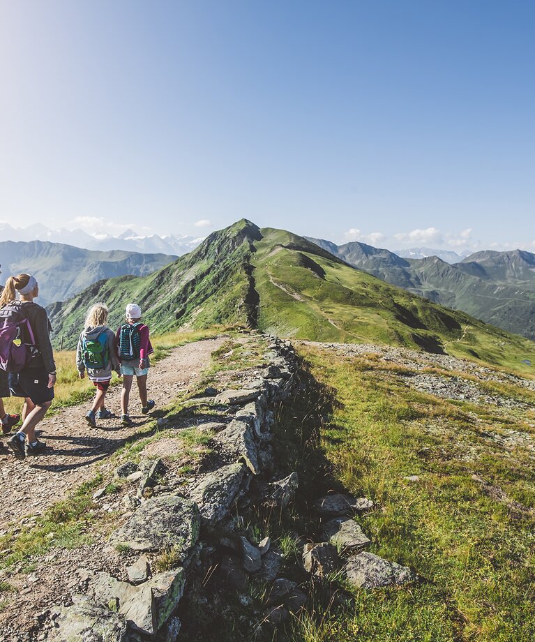 Eine Familie mit zwei Kindern wandert entlang eines Bergpfads | © saalbach.com - Mia Knoll