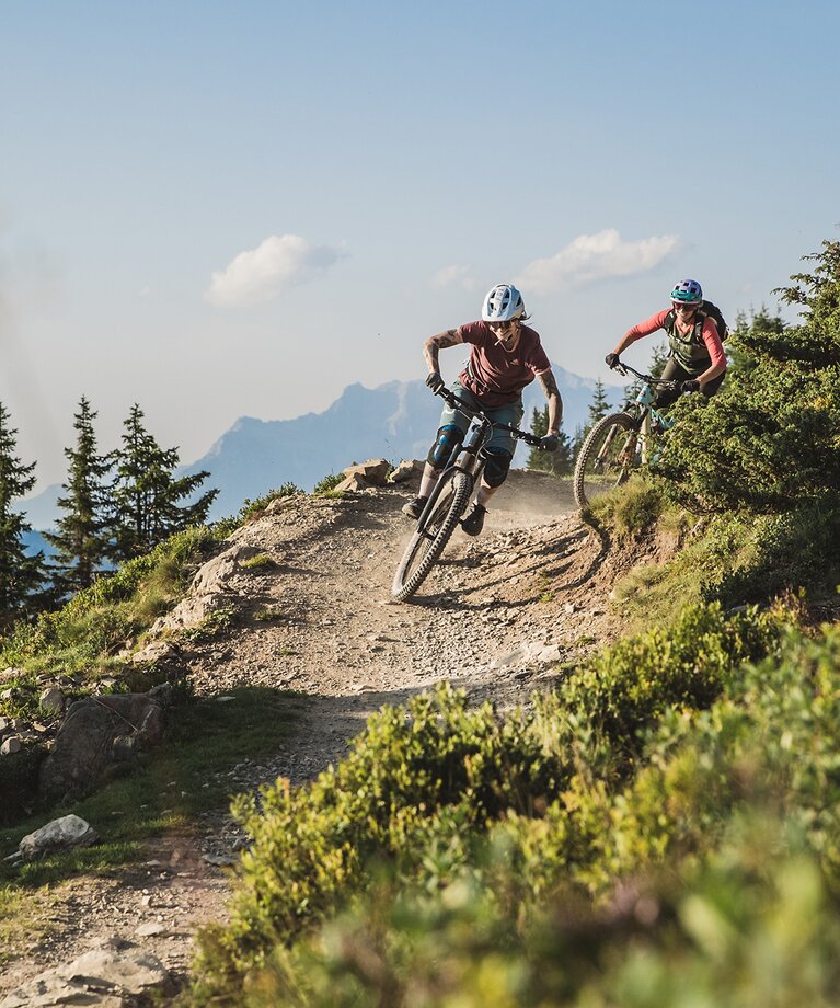 Ein Mountainbiker Pärchen fährt entlang des Hacklbergtrails mit atemberaubendem Bergpanorama | © saalbach.com - Mia Knoll
