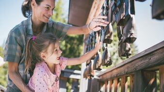 Eine Mutter interagiert mit ihrer Tochter an einer Glocken-Station des Baumzipfelwegs | © saalbach.com - Mia Knoll