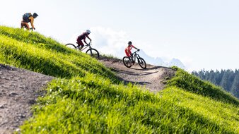Drei Mountainbiker fahren entlang eines Bike-Trails über eine Bergwiese in der Bikearea Fieberbrunn | © saalbach.com - Klemens König