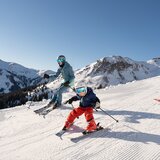 Eine Familie mit Kind auf der Skipiste bei strahlender Sonne im Skicircus Saalbach Hinterglemm | © saalbach.com - Lukas Pilz