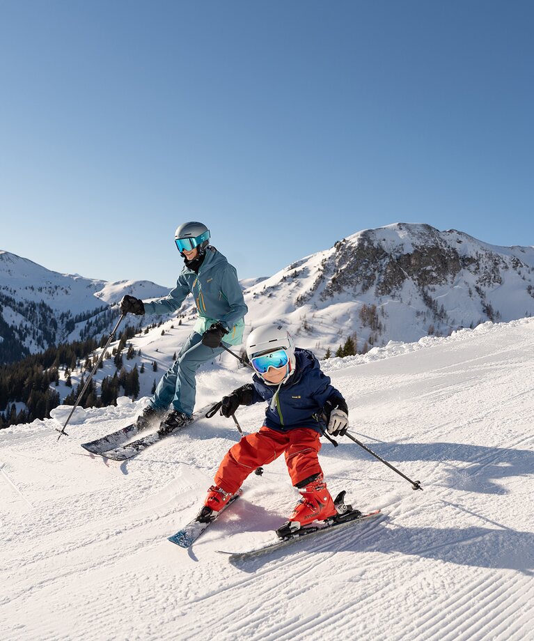Eine Familie mit Kind auf der Skipiste bei strahlender Sonne im Skicircus Saalbach Hinterglemm | © saalbach.com - Lukas Pilz