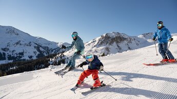 Eine Familie mit Kind auf der Skipiste bei strahlender Sonne im Skicircus Saalbach Hinterglemm | © saalbach.com - Lukas Pilz