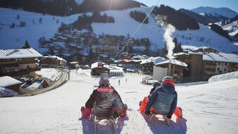Eine Familie mit Kindern beim Rodeln auf einer Skipiste in Saalbach Hinterglemm | © saalbach.com - Daniel Roos