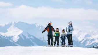 Eine skifahrende Familie mit zwei Kindern steht in einer Reihe auf einer Skipiste | © saalbach.com - Mia Knoll