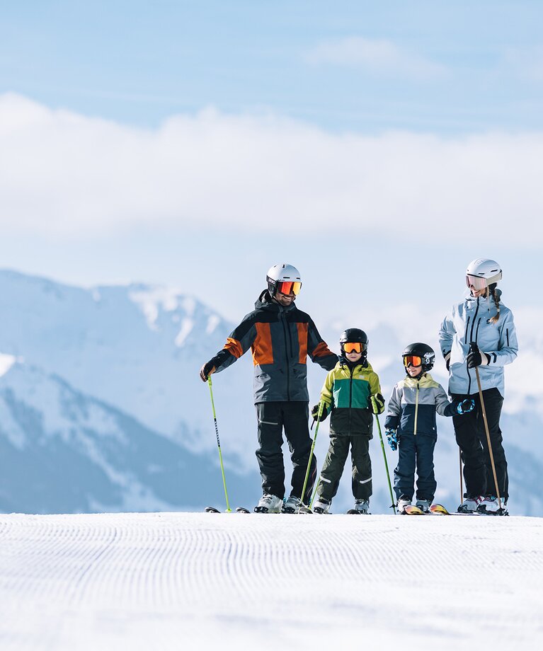 Eine skifahrende Familie mit zwei Kindern steht in einer Reihe auf einer Skipiste | © saalbach.com - Mia Knoll
